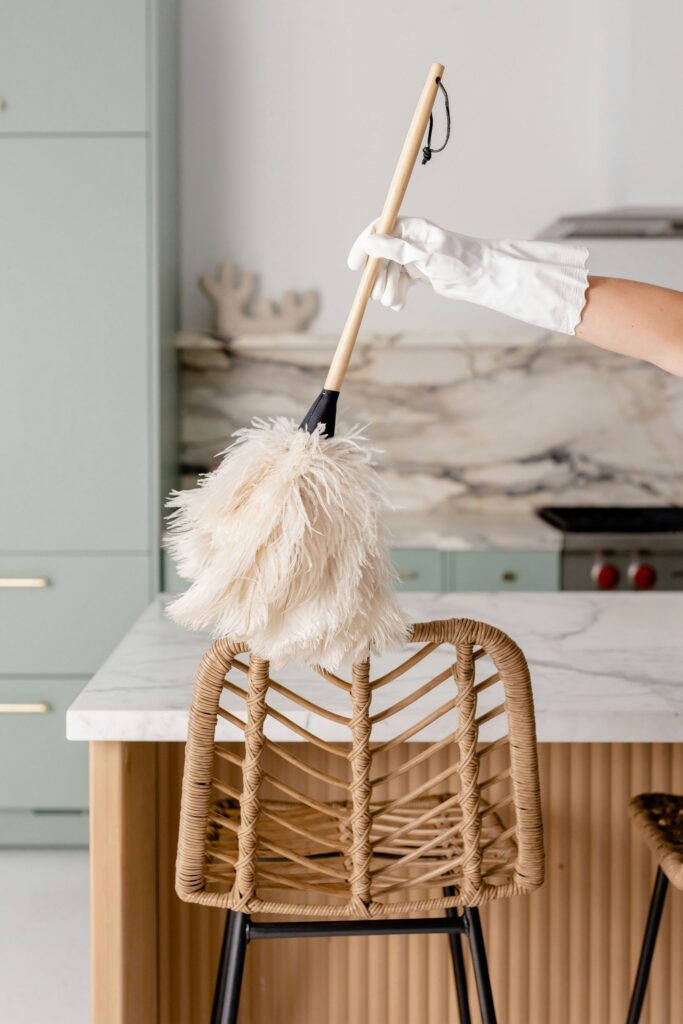 A gloved hand holding a duster, dusting furniture in a kitchen for home cleaning